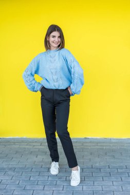 Sarı duvarda mavi kazaklı, gülümseyen güzel kadın portresi.