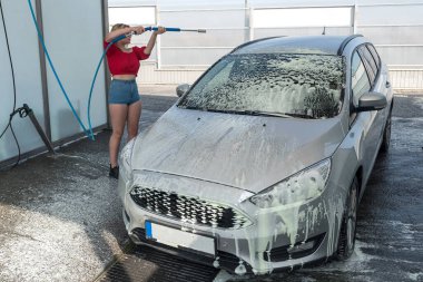 Arabasını sprey köpükle temizleyen genç bir kadın ve çamurdan temizlenen manuel arabada tazyikli su.