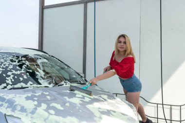 Kadın sürücü beyaz köpüklü teleskopik fırçayla arabasını temizliyor. 