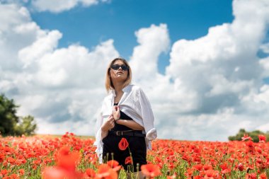 Güzel bayan, güneşli bir günde, kırmızı haşhaş tarlasında boş zamanın tadını çıkarıyor. Sağlıklı yaşam tarzı