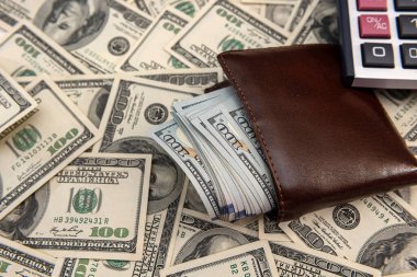 100 dolarlık banknot dolu cüzdan. İş geçmişi olarak hesap makinesi var. Tasarruf kavramı olarak.