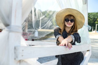 Genç bayan yazın beyaz çardakta gölün yanında poz veriyor.