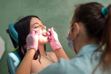 Doktor, hastanın dişini lamba ve aletlerle muayene ediyor. .