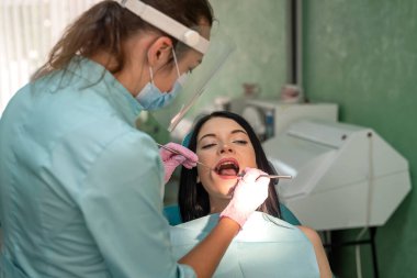 Profesyonel dişçi, aletleri ve koruyucu üniforması ile hastanın dişini tedavi ediyor.