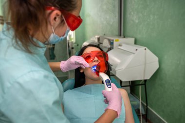 Ağzı açık bir hasta koruyucu gözlüklü bir dişçi koltuğunda oturuyor.