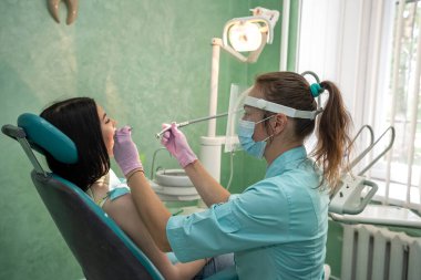Dişçi koltuğundaki kadın dişini acısız tedavi ediyor.