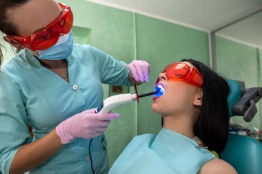 Ağzı açık bir hasta koruyucu gözlüklü bir dişçi koltuğunda oturuyor.