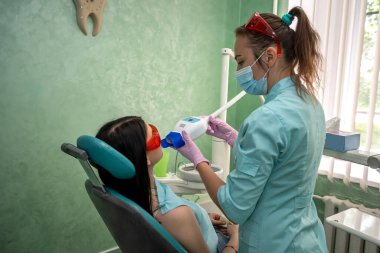 Dişçi koltuğunda oturan genç bir kadın doktorların kontrolü altında beyazlatma prosedürü uyguluyor.
