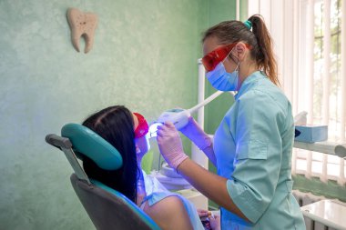 Diş hekimi hasta dişlerini ultraviyole lambayla inceliyor.