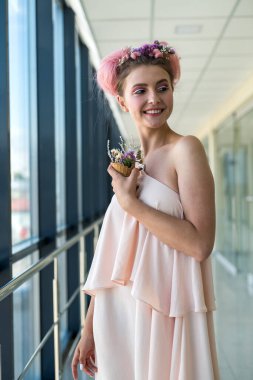 Taze makyajlı güzel bir kadın pencerenin yanında çiçeklerle poz veriyor.