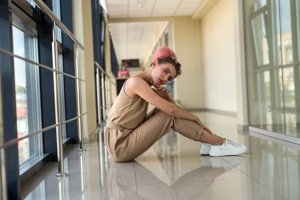 Koridorda yerde oturmuş kameraya poz veren genç bir kadın. 