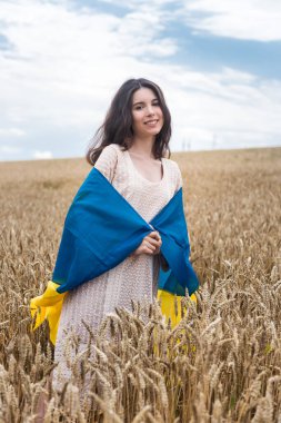 Ukrayna bayrağı taşıyan bir kız ve olgun buğday tarlasında yürüyor. Ukrayna 'da barış. Yaşam tarzının tadını çıkar