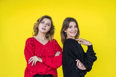 Sarı duvar stüdyo resmine izole edilmiş modern örgü süveterlerle poz veren genç kızlar.