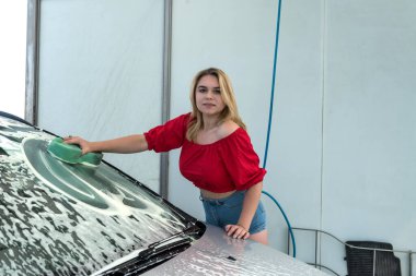 Güzel bir kadın arabasını köpüklü yeşil süngerle yıkıyor. 