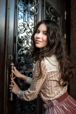 Genç ve güzel bir kadının portresi eski dokuma kapılarının yanında poz veren bir elbise giyiyor. 