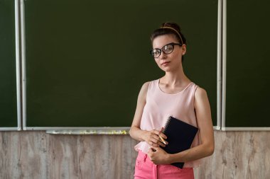 Genç öğretmen boş tahtanın yanında duruyor ve yeni bir ders veriyor.