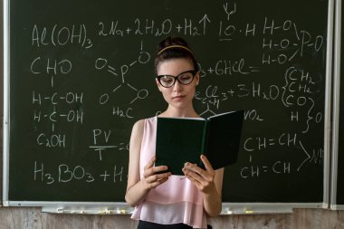 Bayan öğretmen kimyasal formülleri karatahta ve eğitim konseptinin yanında açıklıyor.