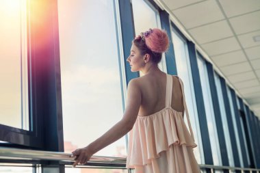 Taze makyajlı güzel bir kadın pencerenin yanında çiçeklerle poz veriyor.