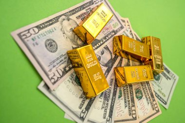 Parlak yeşil arka planda üzerinde altın külçeler olan banknotlar uzanır. İş konsepti