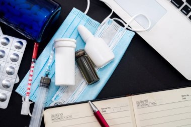 Siyah bir arka planda dizüstü bilgisayar, defter, kalem, hap, şırınga, maske, damla, bütil tablet var. Tıp konsepti