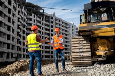 İnşaat halindeki binanın arka planına karşı, önlüklü iki genç işçi sırtlarını dönerek yeni binaya bakıyorlar. İnşaat konsepti.