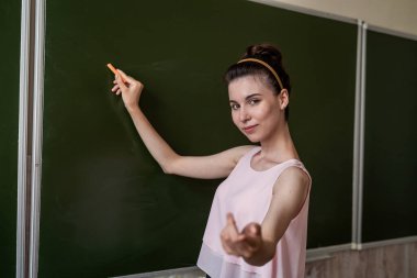 Genç öğretmen boş tahtanın yanında duruyor ve yeni bir ders veriyor.