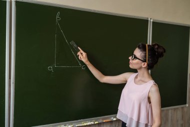 İlkokul öğretmeni tahtaya yakın bir üçgen çiziyor.