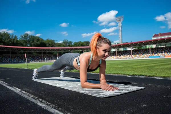 Genç spor giyim koçu yoga yapıyor ve stadyumda esneme egzersizleri yapıyor.