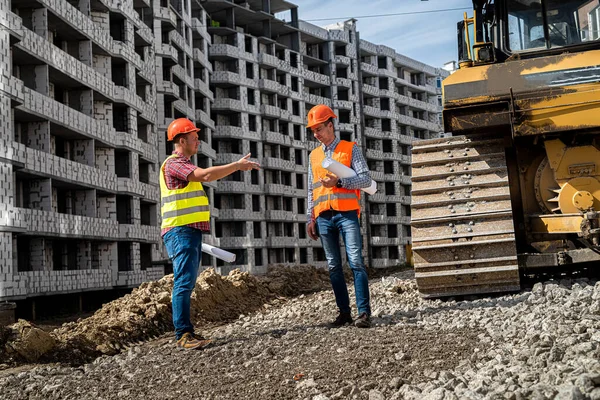 İnşaat halindeki binanın arka planına karşı, önlüklü iki genç işçi sırtlarını dönerek yeni binaya bakıyorlar. İnşaat konsepti.