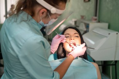 Dişçi sandalyesinde stomatolojik ayna olan hastanın dişine bakıyor.