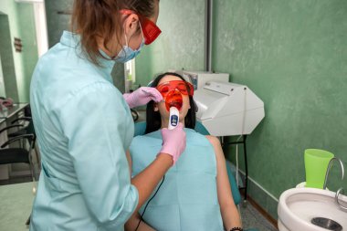 Dişçi koltuğundaki kadın dişini acısız tedavi ediyor.