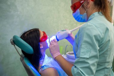 Dentist with ultraviolet lamp in dentistry making whitening to a patien