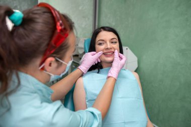 Kadın dişçi elleri hastanın ağzını, dişçi muayenehanesini muayene eder.