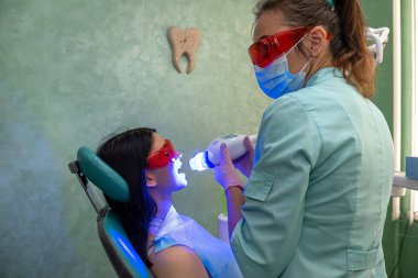 Kadın dişçi, dişçi hastasını ultraviyole lamba kullanarak dolduruyor. Diş beyazlatma prosedürü