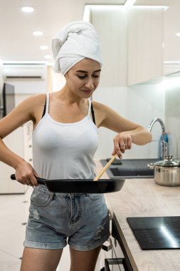 Beyaz havluya sarılı bir duştan sonra genç ev hanımı mutfakta duruyor ve kahvaltıyı bir tavaya hazırlıyor.