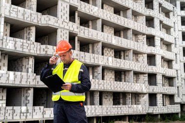Üniformalı ve kasklı bir işçi yeni binanın arka planında tabletine bakıyor. İnşaat konsepti