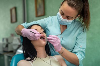 Profesyonel dişçi, aletleri ve koruyucu üniforması ile hastanın dişini tedavi ediyor.