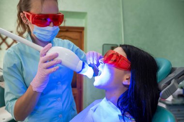 Dentist with ultraviolet lamp in dentistry making whitening to a patien