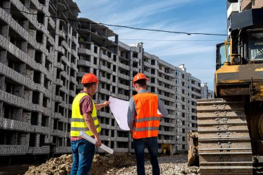 İnşaat alanında üniformalı iki güzel işçi bir plan düşünüyor. İnşaat malzemeleri