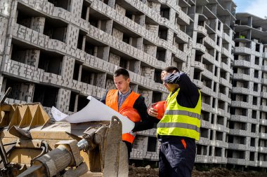 Bir inşaat alanında, üniformalı bir işçi üniformalı bir işçiye evin planını gösteriyor. İnşaat konsepti