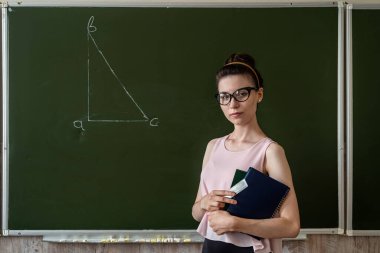 İlkokul öğretmeni tahtaya yakın bir üçgen çiziyor.