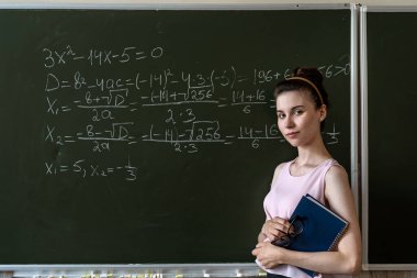 liseli kız karatahtaya tebeşirle matematik formülü yazıyor, matematik sınıfı cebiri.