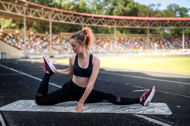 Sağlıklı bir kadın, stadyumun dışında paspasın üzerinde geriniyor. Sağlıklı yaşam tarzı kas esnekliği kavramı