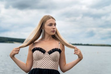 Gökyüzü ve suyun arka planında uzun siyah elbiseli güzel genç bayan, özgürlük.