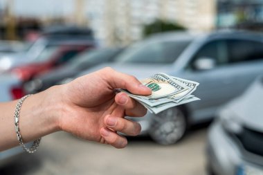 Man buys a modern car, holding dollar against auto in back. sale concept