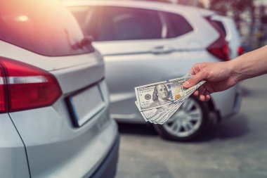 Man buys a modern car, holding dollar against auto in back. sale concept