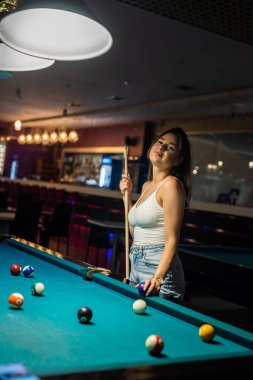 Genç mutlu kız elinde ıstakayla barda bilardo oynuyor. Yaşam biçimi