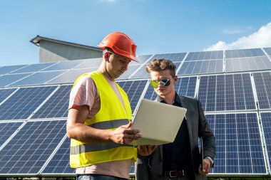 Patron ve çalışanı güneş panellerinin yanında duruyorlar.