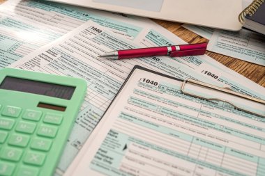 Vergi, yeni ahşap bir masanın üzerinde duran kalem hesap makinesiyle bir tablet üzerinde 1040 formu oluşturur. Belgelendirme kavramı