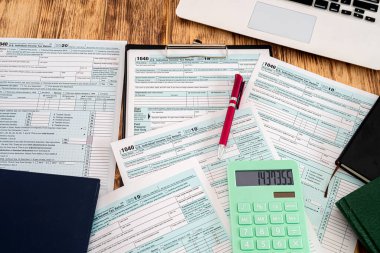 Kullanışlı defterler kırmızı kalem ve vergi formları ile ahşap masaya saçılmış 1040 USA. Belgelendirme kavramı